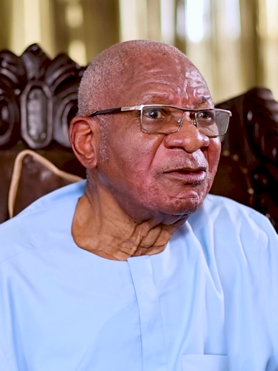 Prof. Imevbore seated in a carved chair at home, speaking to camera